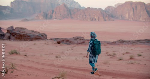 4K slow motion orbit shot of young Caucasian woman in turban walking away on red sand in Wadi Rum desert, Jordan. Captures solitude, movement, and travel spirit in a timeless natural setting