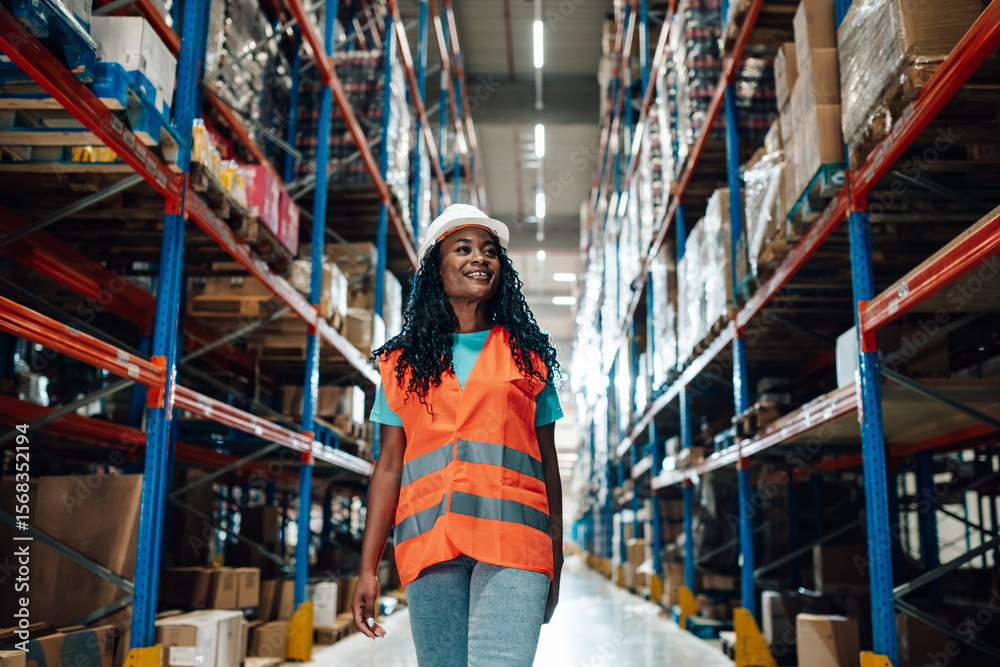 Fototapeta premium Smiling female supervisor walking through retail warehouse with packed shelves