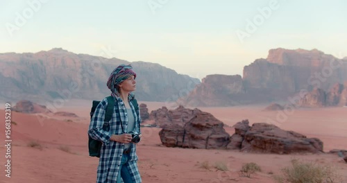 Tourist woman in turban walks in Wadi Rum desert and takes pictures with Analog photo camera. Timeless spirit of travel, cultural exploration, and vintage storytelling. 4K Slow motion gimbal shot