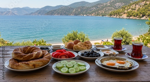 Fototapeta Naklejka Na Ścianę i Meble -  Turkish breakfast feast with simit, eggs, olives, and tea overlooking the Aegean Sea