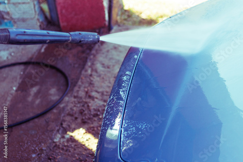 Car washing with high-pressure water spray at an outdoor facility on a sunny day