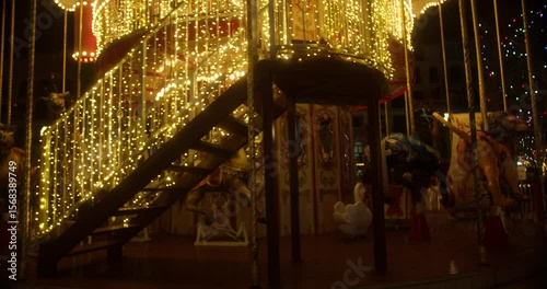 The illuminated carousel in the amusement park is spinning at night. The beautiful park is having fun