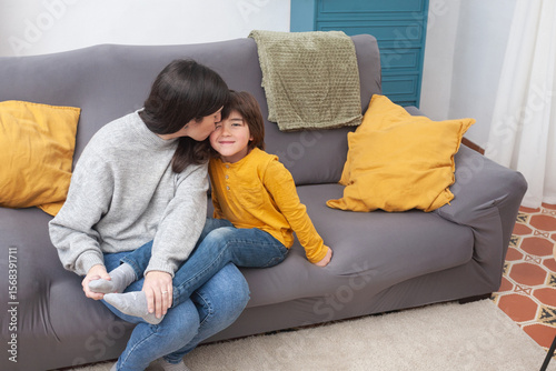 Mother kisses smiling child while pulling off socks on sofa