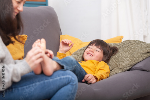 Laughing boy gets feet tickled by mother on cozy sofa
