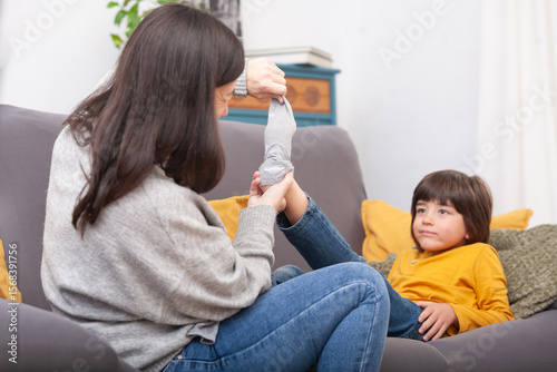 Mother pulling sock off relaxed son's foot on sofa
