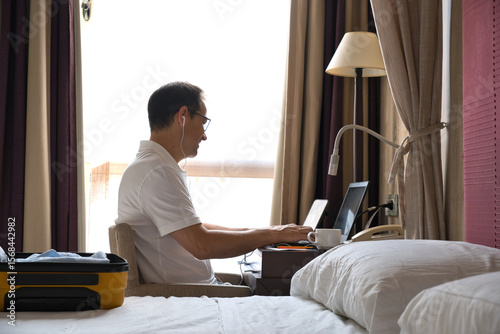 A salesman on a business trip connected to a video call at his hotel with a laptop computer.
