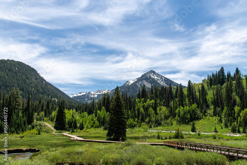 Panoramic view over the Donut Falls Boardwalk, green mountains and feather clouds in sky in Big Cottonwood Canyon with trail to a Donut Falls waterfall just outside Salt Lake City, UT, USA