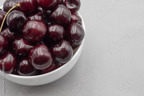 Fresh dark cherries in ceramic bowl on neutral gray cloth – minimal food photography