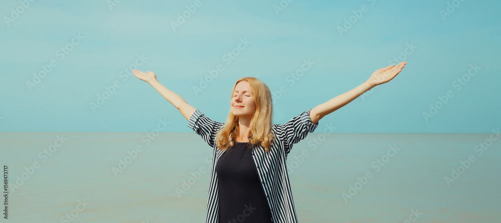 Obraz premium Summer vacation, happy inspired young woman raising her hands up on the beach, relaxed girl on sea