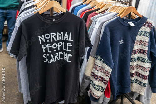 Murais de parede London, UK, 9 May 2025 Clothes on a Rack at an Outdoor Market, Featuring a Humorous T-shirt