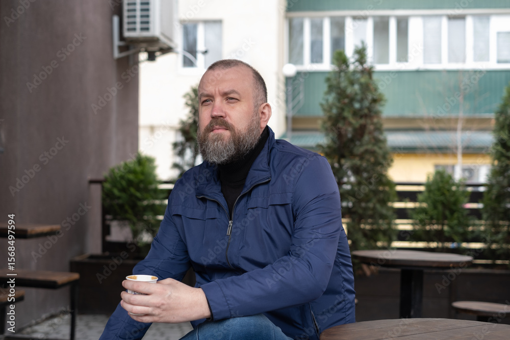 Fototapeta premium Man enjoying coffee outside a cafe during daytime in a modern urban setting with trees around