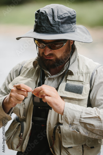 Fisherman tying fly on fishing line while wearing fishing vest and hat