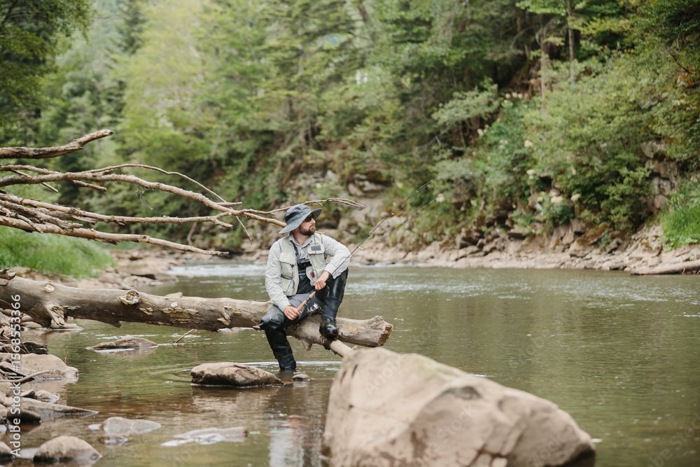 Fisherman sitting on fallen tree trunk, enjoying trout fishing in river Fisherman sitting on fallen tree trunk, enjoying trout fishing in river