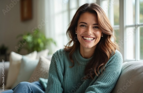 Portrait of happy brunette woman with perfect white teeth smiling cheerfully indoors. Wears cozy sweater, sitting comfortably on sofa near window. Natural, youthful expression conveys happiness, Free Download Portrait of happy brunette woman with perfect white teeth smiling cheerfully indoors. Wears cozy sweater, sitting comfortably on sofa near window. Natural, youthful expression conveys happiness, - GFXLoad