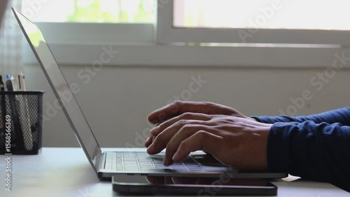 Close-up of a male freelancer's hands typing on laptop keyboard while working remotely. Modern work lifestyle on digital technology, flexibility, freelance, online business, remote job at home office.