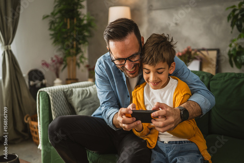 Father and son play video games on a mobile phone and enjoy at home