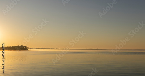 An early morning view along the Pasquotank River with calm water and mist on the distant surface