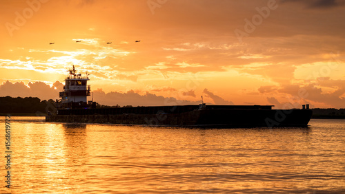 Cuadro en lienzo A barge going down the river at sunset with 4 helicopters silhouetted against th