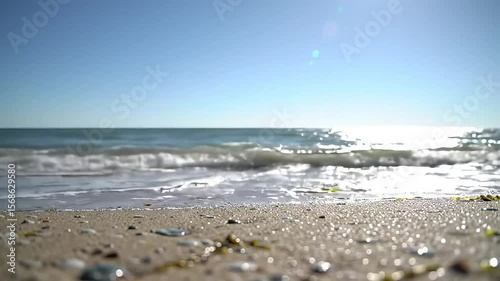Ocean waves gently meet the sandy shore under a clear sunny sky capturing a tranquil beach scene