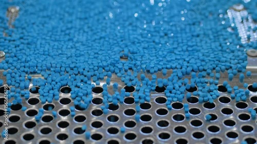 Close up: blue recycled plastic granules, pellets on vibrating shale shaker, conveyor belt for separating, sorting material - plastic recycling machine. Reuse, waste reduction and sustainable concept