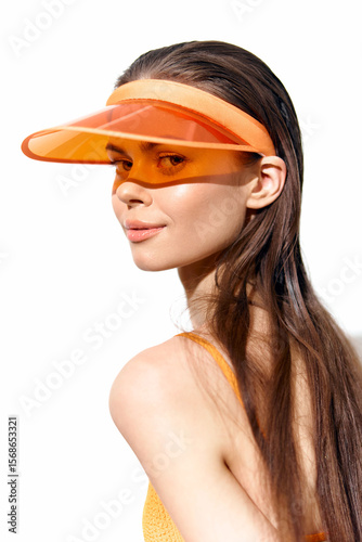 Stylish young woman in an orange visor and swimwear, exuding confidence and summer vibes. Bright colors enhance the summertime feel with a modern touch.