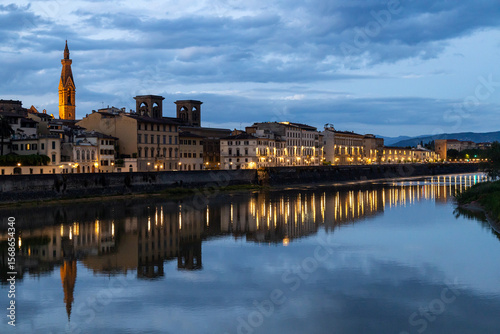 Fototapeta Naklejka Na Ścianę i Meble -  Illuminated buildings along the Arno River reflecting on the water during blue hour in Florence city center, Italy