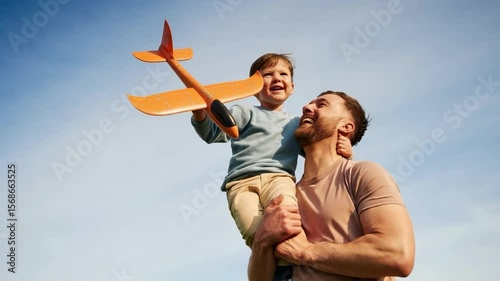 A father and son share a joyful moment, playing with a toy airplane under a bright sky.