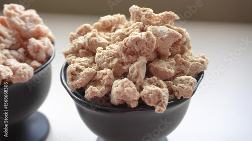 two black bowls with soaked soy meat and dry. On the left is a bowl with pieces of dry soy with a looser and more porous consistency. Soaked soy meat on the right.