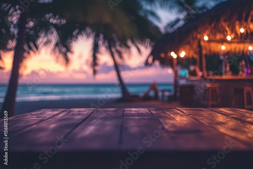 Fototapeta Naklejka Na Ścianę i Meble -  Wooden table on a beach at sunset with a beach bar in the background.
