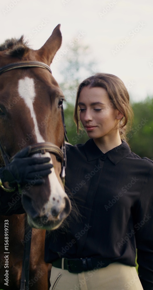 Fototapeta premium An elegant woman strokes a horse's muzzle and poses looking at the camera