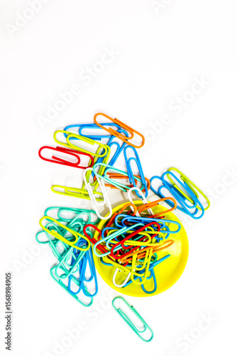 Vibrant assortment of colorful paper clips spilling from a bright yellow container