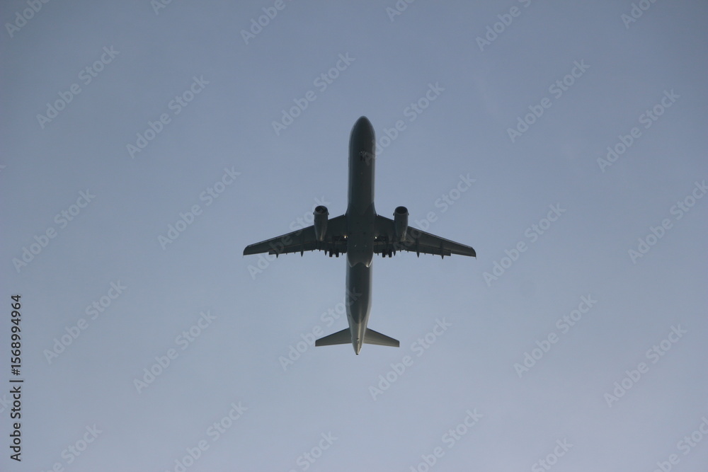 Fototapeta premium Una impresionante vista de un avión tomada desde abajo contra un cielo azul despejado. La aeronave luce elegante y moderna, simbolizando los viajes, la aventura y el espíritu explorador. Viajes