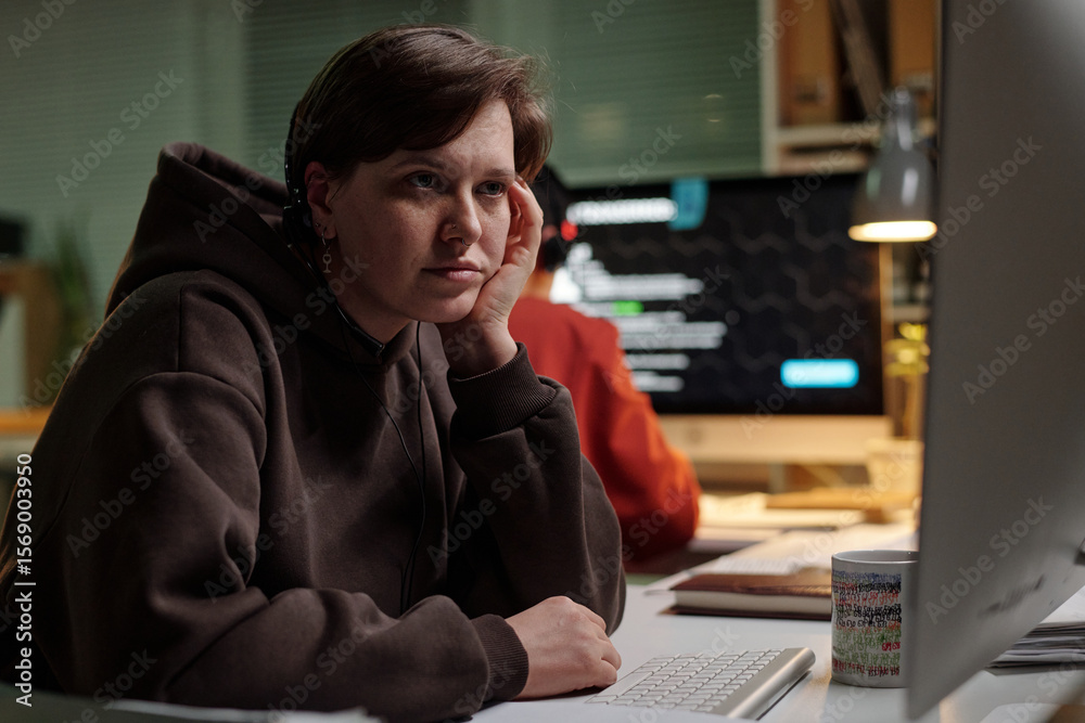 Caucasian young adult woman sitting at desk using computer, resting chin on hand, looking at monitor with scam call center interface visible on screen Caucasian young adult woman sitting at desk using computer, resting chin on hand, looking at monitor with scam call center interface visible on screen