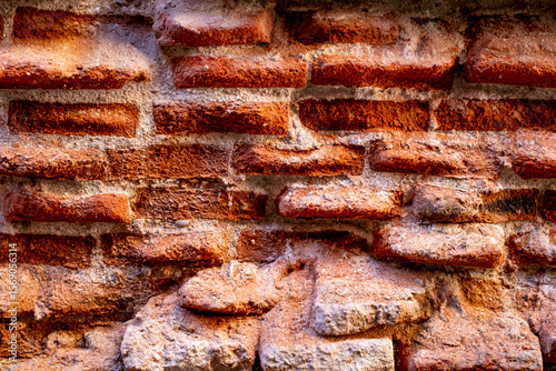 A close-up of a beat-up red brick wall with rough, uneven bricks in shades of red, orange, and brown, showing off years of wear and tear.