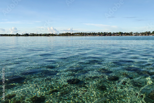 Crystal-clear turquoise waters with coral reef visible beneath the surface, with the coastline of Semporna, Sabah in the background.