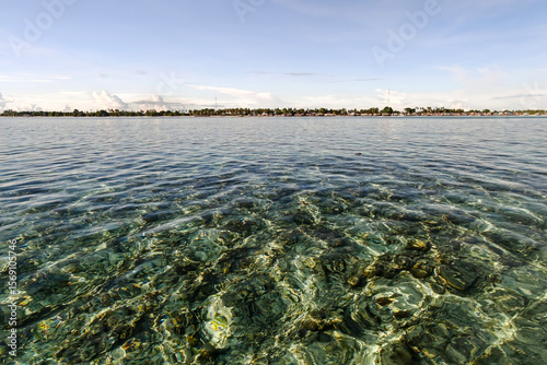 Crystal-clear turquoise waters with coral reef visible beneath the surface, with the coastline of Semporna, Sabah in the background.