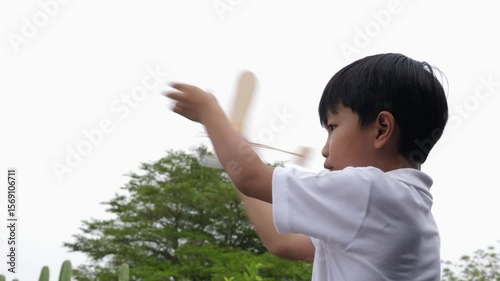 Asian child boy play airplane toy outdoor with fun face in nature background. Happy kid in white shirt enjoy playing in relaxing day.