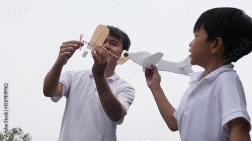 Happy family asian child boy and father play airplane toy outdoor together with fun face in nature background. Happy kid and dad in white shirt enjoy playing in relaxing day.