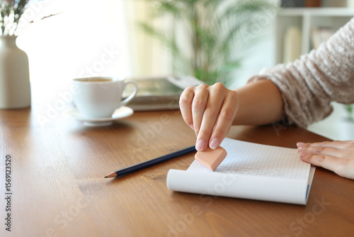 Woman hand using rubber erasing text on a wooden table at home