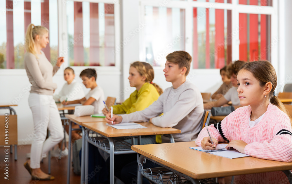 Fototapeta premium Teenagers sitting at desks in classroom during lesson and doing tasks.
