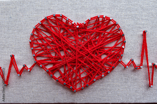 Red heart and heartbeat lines string art made with tangled red yarn on metal nails at canvas texture. Valentines Day gift