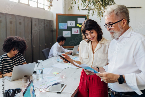 Businesswoman with smart phone reviewing report with manager at office