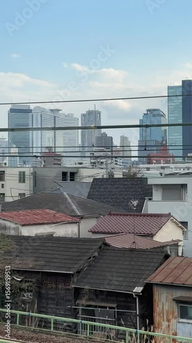 Modern residential houses with sleek architecture in Tokyo, Japan, viewed from a train platform.  A cityscape of skyscrapers forms a striking backdrop.