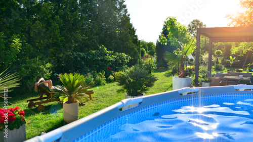 Modern aluminum pergola with stylish garden furniture in a beautiful garden. Swimming pool with metal frame for home and garden. Frame swimming pool in the yard. 