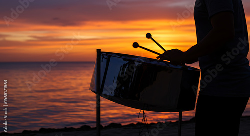 Silhouetted steelpan player performs at sunset by the ocean, creating a vibrant tropical scene.