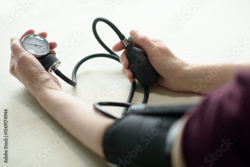 An elderly woman living alone takes charge of her health by checking her blood pressure at home using a manual monitor. Self-care and independent aging in daily life.