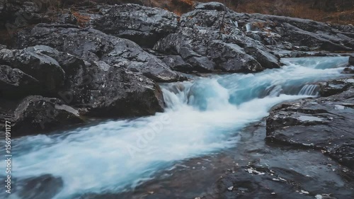 Flowing water creates a beautiful blue stream amidst rugged rocks in a tranquil natural setting at dusk