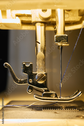 Close-up view of sewing machine needle and presser foot with blue thread