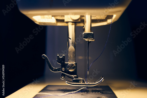Close-up of sewing machine needle and presser foot with thread under warm lighting