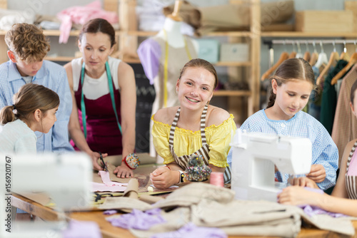 Girl child watches female classmates work on creating clothes, school for young fashion designers and tailors. Children practice sewing, learn new skills.